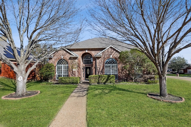 traditional-style home featuring a shingled roof, a front yard, and brick siding