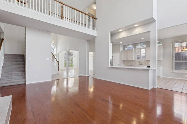 unfurnished living room with stairs, wood finished floors, a towering ceiling, and baseboards