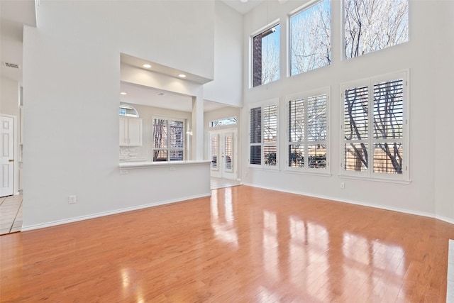 unfurnished living room with recessed lighting, visible vents, a towering ceiling, wood finished floors, and baseboards