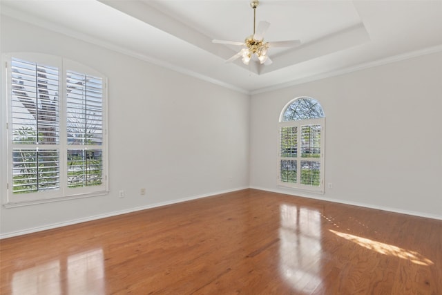 spare room featuring a tray ceiling, wood finished floors, a ceiling fan, and baseboards