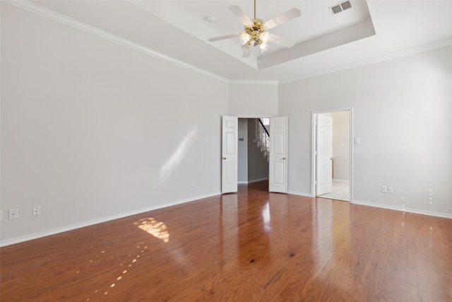 unfurnished room with ceiling fan, wood finished floors, visible vents, baseboards, and a tray ceiling