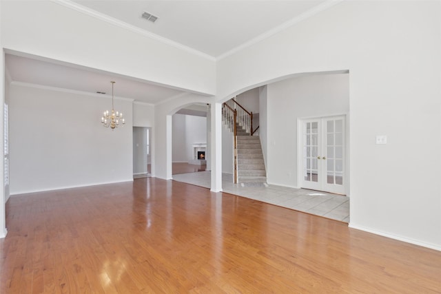 unfurnished living room with visible vents, an inviting chandelier, wood finished floors, a lit fireplace, and stairs