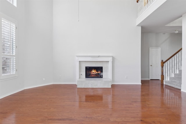 unfurnished living room with a fireplace, wood finished floors, a towering ceiling, baseboards, and stairway