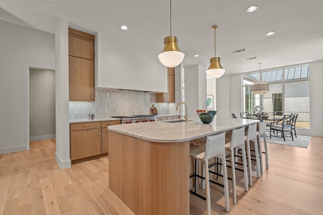 kitchen featuring a sink, light countertops, stainless steel gas stovetop, light wood finished floors, and tasteful backsplash