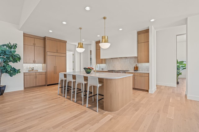 kitchen with a breakfast bar area, light countertops, light wood-style flooring, a sink, and premium range hood