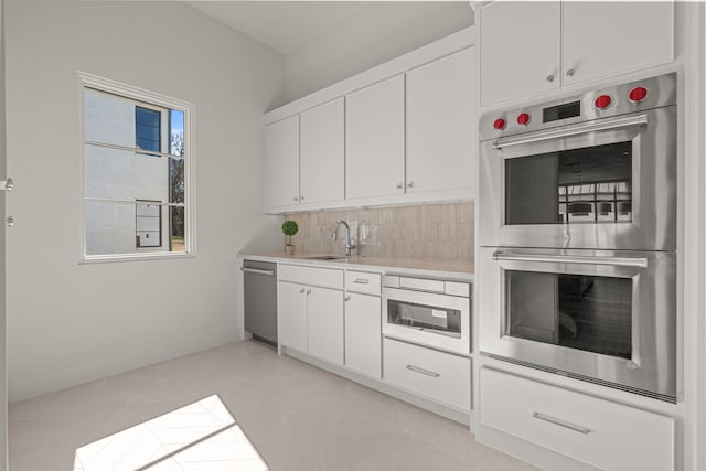 kitchen with stainless steel appliances, light countertops, decorative backsplash, white cabinets, and a sink