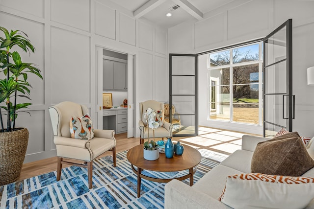 living area with coffered ceiling, a decorative wall, beam ceiling, and light wood finished floors