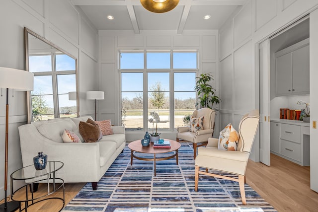 living area with light wood-type flooring, coffered ceiling, a decorative wall, and beamed ceiling