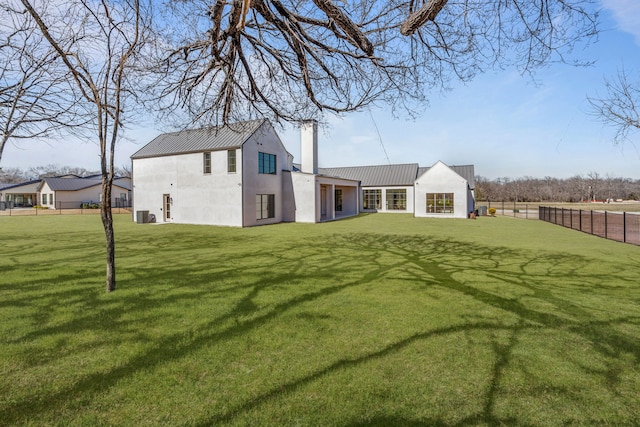 back of house with a chimney, fence, metal roof, and a lawn