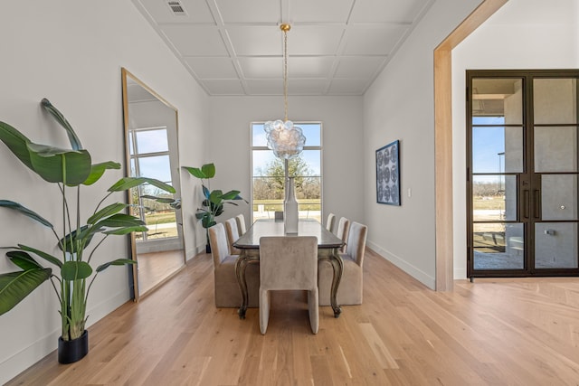 dining space with light wood-type flooring, baseboards, visible vents, and a notable chandelier