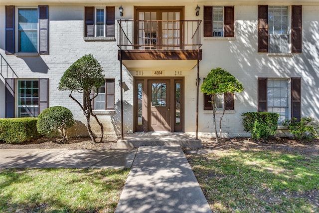 view of exterior entry featuring brick siding and a balcony