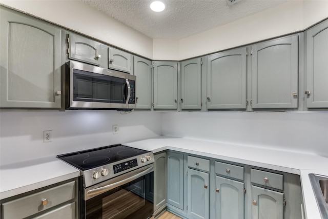 kitchen featuring light countertops, light wood-style flooring, appliances with stainless steel finishes, a sink, and a textured ceiling