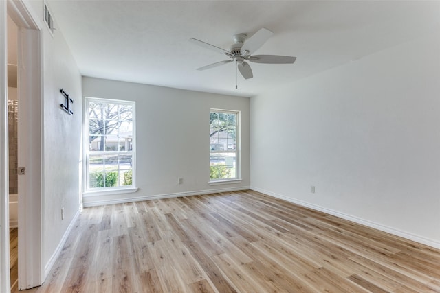 empty room featuring light wood-type flooring, a healthy amount of sunlight, visible vents, and baseboards