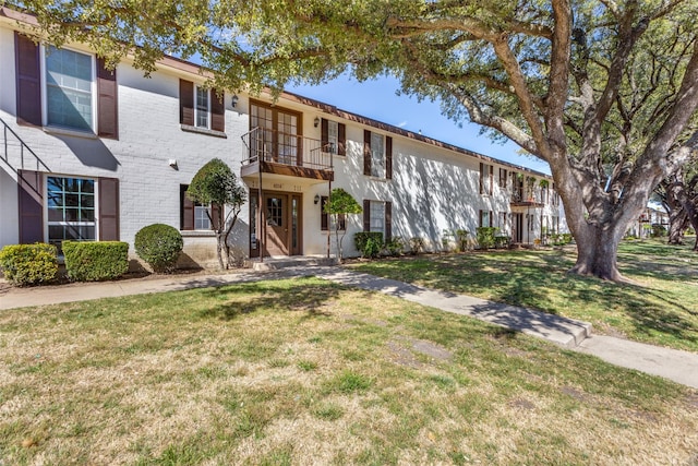 multi unit property with brick siding, a front yard, and a balcony