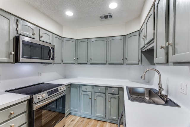 kitchen with a textured ceiling, stainless steel appliances, a sink, light countertops, and light wood finished floors