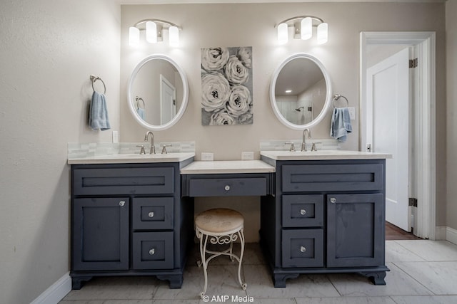 full bath featuring a sink, marble finish floor, baseboards, and two vanities