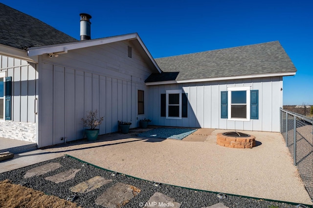 rear view of house with an outdoor fire pit, fence, board and batten siding, and roof with shingles