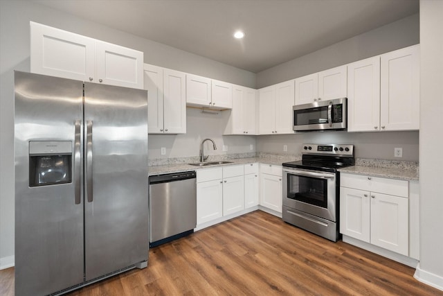 kitchen with dark wood-type flooring, a sink, white cabinets, appliances with stainless steel finishes, and light stone countertops