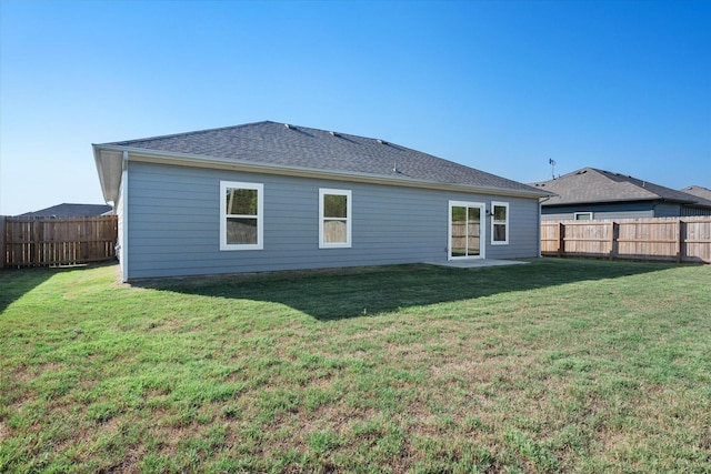 back of property with a fenced backyard, a shingled roof, and a lawn