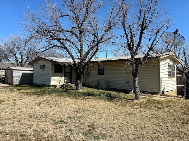 rear view of property featuring central AC, an outdoor structure, a lawn, and a storage unit