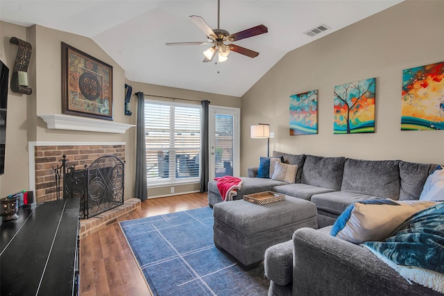 living room with lofted ceiling, a brick fireplace, visible vents, and wood finished floors