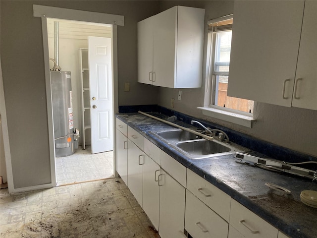 kitchen with white cabinets, dark countertops, light floors, water heater, and a sink