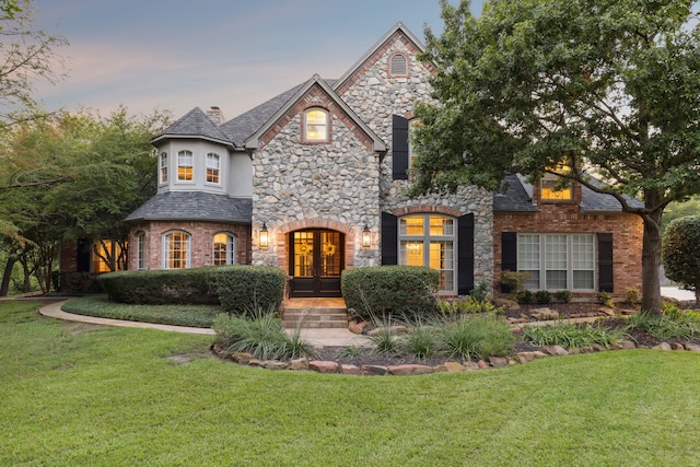 french provincial home with a yard, stucco siding, and french doors