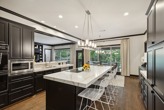 kitchen with stainless steel microwave, a breakfast bar, ornamental molding, a center island, and a sink