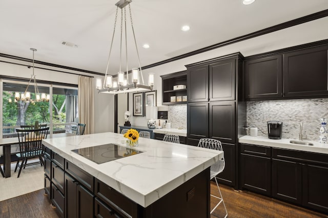 kitchen featuring black electric cooktop, a kitchen island, visible vents, a sink, and crown molding