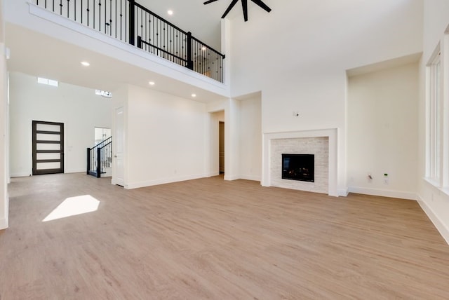 unfurnished living room featuring light wood finished floors, a towering ceiling, a glass covered fireplace, baseboards, and stairs