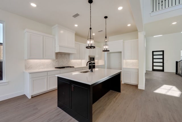 kitchen featuring light countertops, stainless steel microwave, a sink, an island with sink, and stovetop