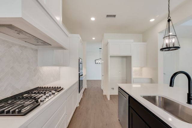 kitchen with premium range hood, a sink, white cabinets, appliances with stainless steel finishes, and decorative light fixtures