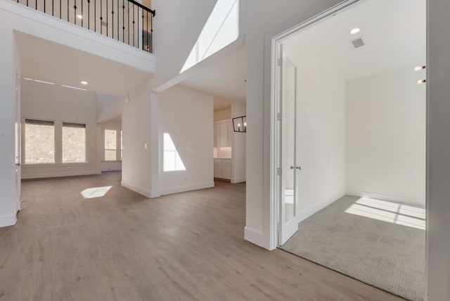 interior space with baseboards, visible vents, a towering ceiling, wood finished floors, and an inviting chandelier