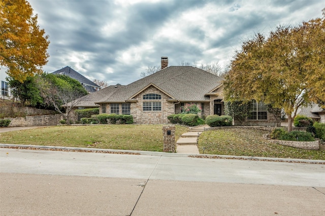 view of front of house with a shingled roof, stone siding, a chimney, and a front lawn