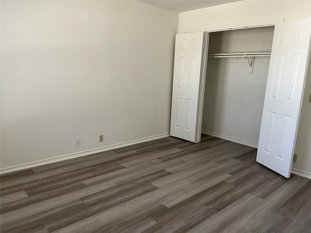 unfurnished bedroom with dark wood-style floors, baseboards, and a closet