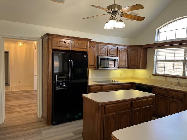 kitchen featuring light wood-style flooring, a kitchen island, a sink, light countertops, and black appliances