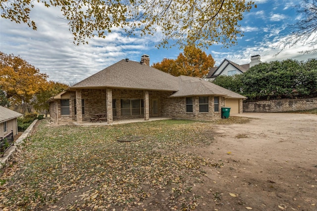 back of house featuring a shingled roof, a patio area, brick siding, and a chimney