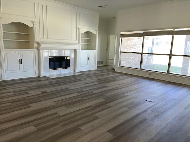 unfurnished living room featuring a fireplace, visible vents, built in features, dark wood-style floors, and crown molding