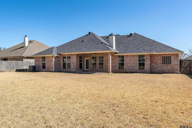 back of house featuring brick siding, roof with shingles, a chimney, and a fenced backyard