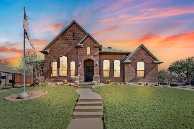 french provincial home featuring a gate, fence, a front lawn, and brick siding