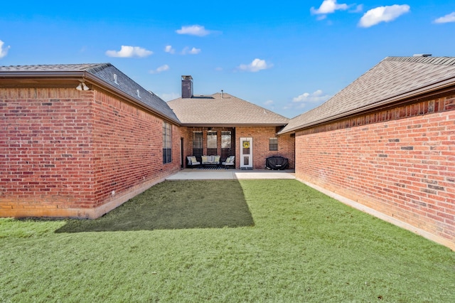 back of property featuring brick siding, a yard, roof with shingles, a chimney, and a patio area