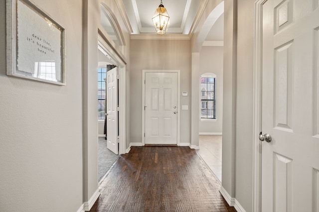 entryway with arched walkways, a chandelier, dark wood-style flooring, baseboards, and ornamental molding