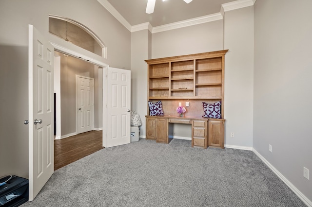 carpeted home office featuring baseboards, built in study area, a towering ceiling, ceiling fan, and ornamental molding