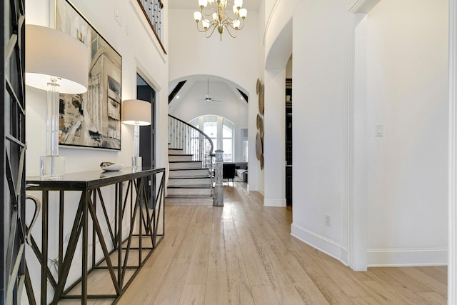 foyer entrance with arched walkways, wood finished floors, a high ceiling, stairs, and a notable chandelier