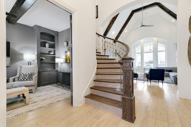 stairway featuring built in shelves, arched walkways, wood-type flooring, high vaulted ceiling, and beamed ceiling