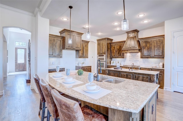 kitchen featuring an island with sink, light wood-style floors, arched walkways, and a sink