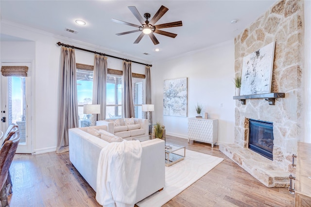 living area with visible vents, crown molding, a stone fireplace, and wood finished floors