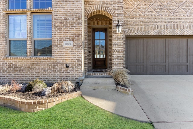 entrance to property with brick siding, driveway, and an attached garage