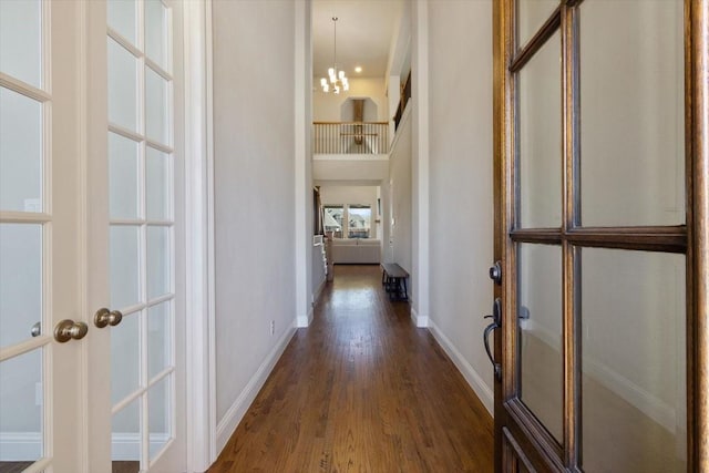 corridor with dark wood-style floors, a towering ceiling, baseboards, and an inviting chandelier