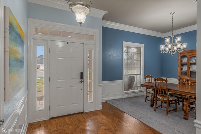 foyer featuring crown molding, a wealth of natural light, wainscoting, and a notable chandelier